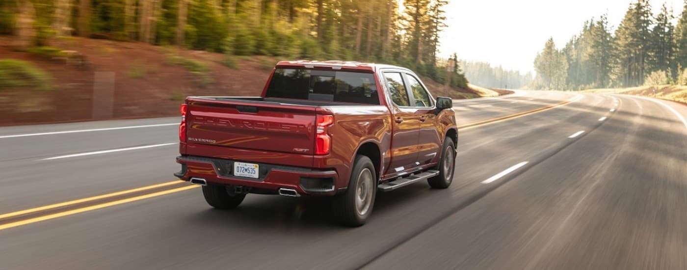 A red 2021 Chevy Silverado 1500 is shown from the rear driving on an open road.