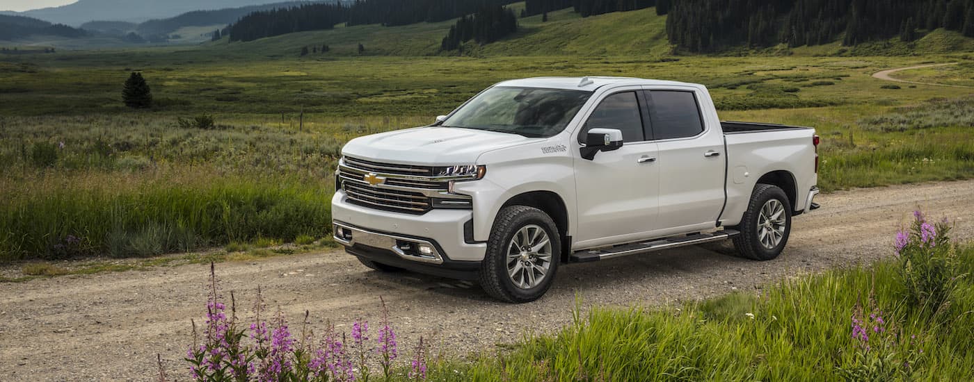 A white 2021 Chevy Silverado 1500 High Country is shown from the side driving past a grassy field.