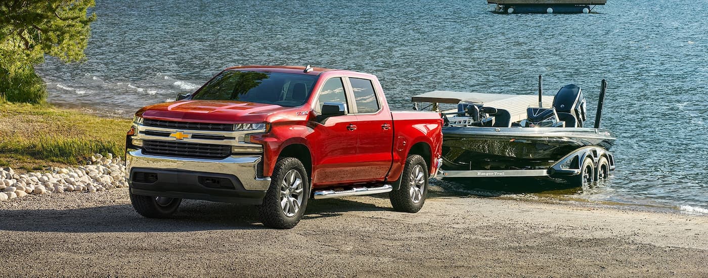 A red 2022 Chevy Silverado 1500 Z71 is shown towing a boat next to a lake.