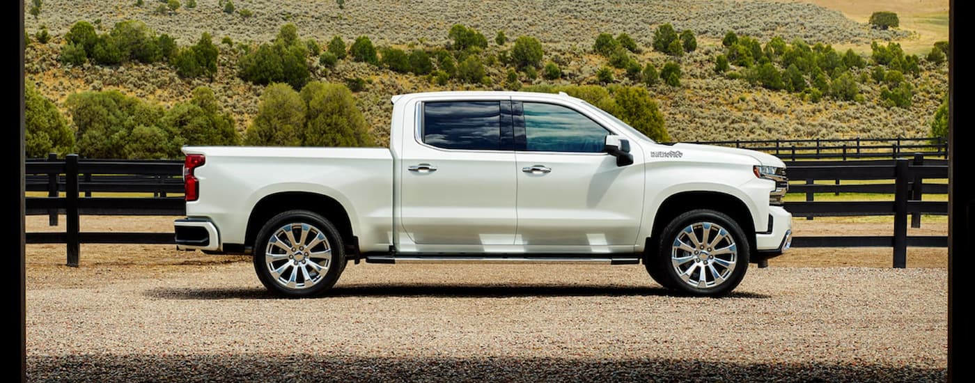 A white 2022 Chevy Silverado 1500 is shown from the side parked in front of a grassy hill.