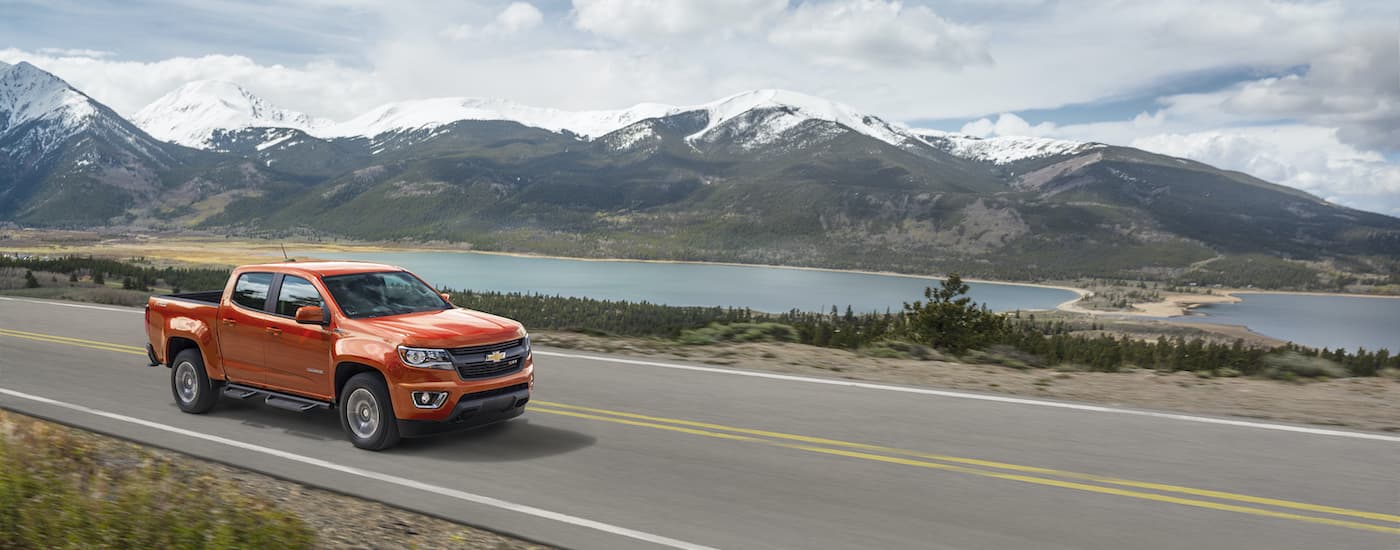 An orange 2016 Chevy Colorado Z71 is shown driving past a river and mountains.