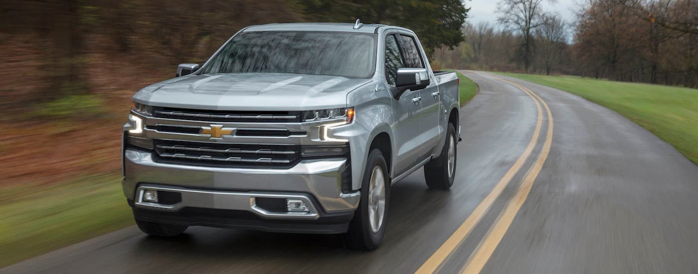 A popular vehicle for Chevy used truck sales, a silver 2019 Chevy Silverado 1500 LTZ, is shown driving on an open road.