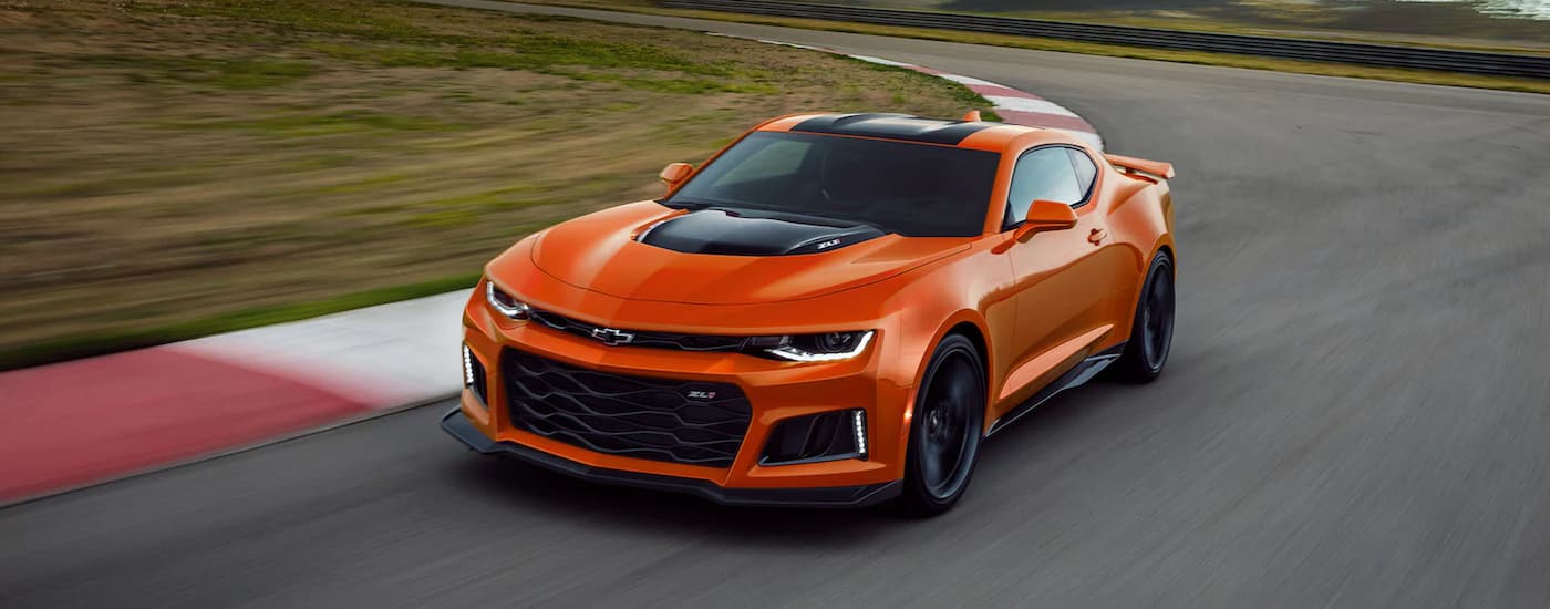 An orange 2022 Chevy Camaro ZL1 is shown driving on a racetrack.
