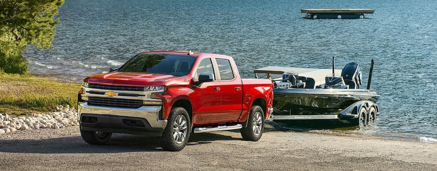 A red 2022 Chevy Silverado 1500 LTD is shown towing a fishing boat out of a lake.