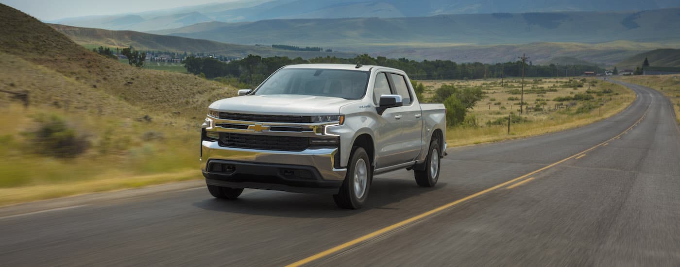 A silver 2019 Chevy Silverado 1500 LT is shown driving past a field.