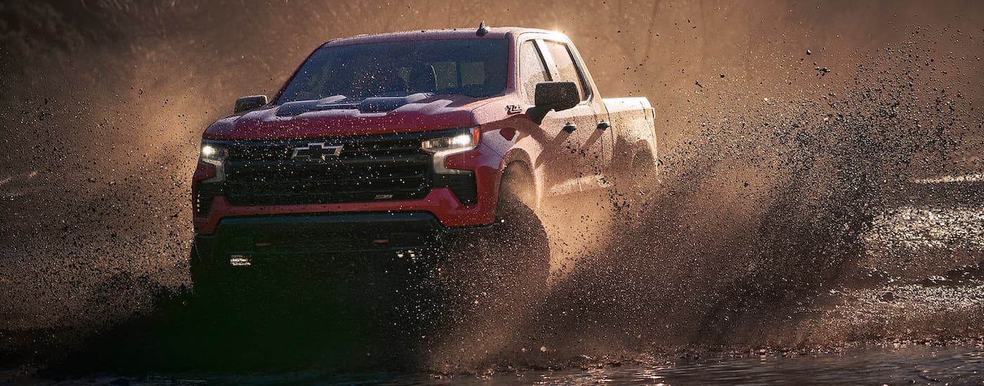 A red 2022 Chevy Silverado 1500 Z71 is shown driving through mud after leaving a Miami used truck dealership.