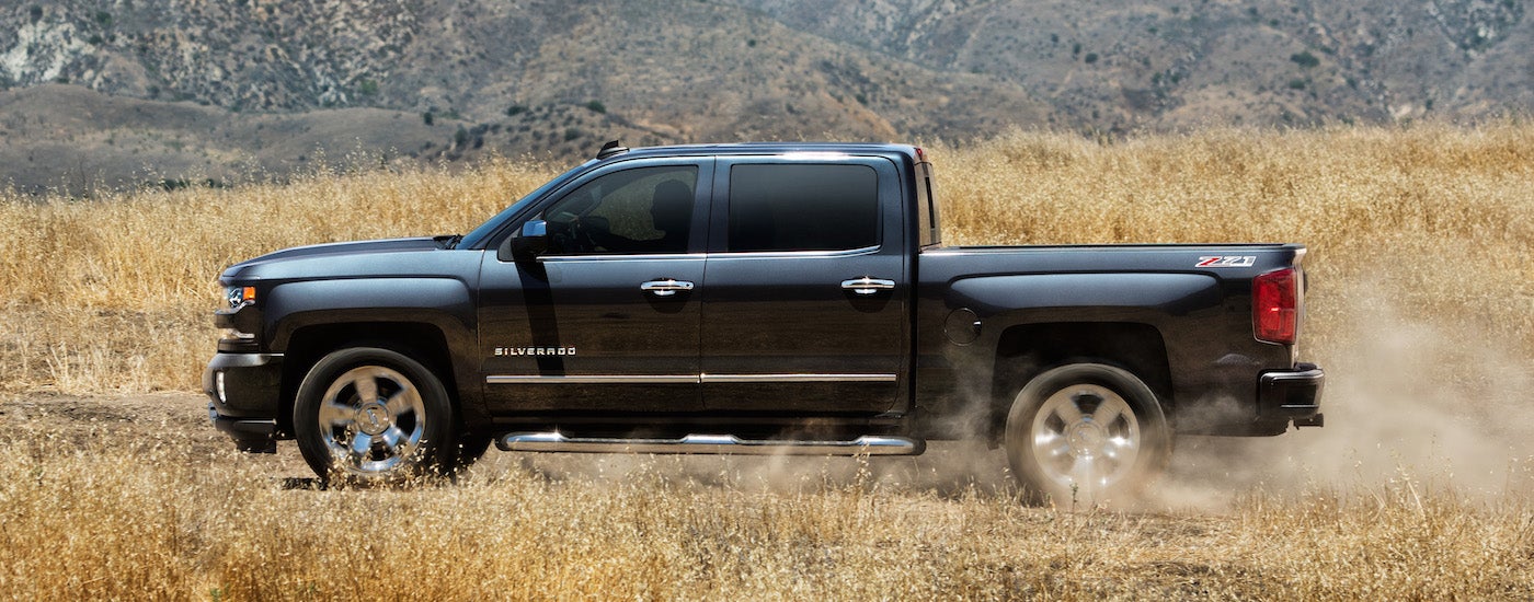 A black 2018 Chevy Silverado is shown from the side parked in a dry grassy field.