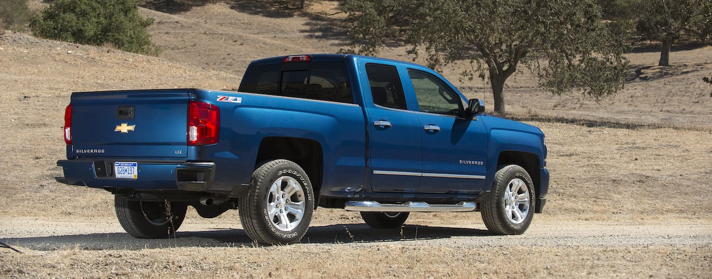 A blue 2017 Chevy Silverado 1500 is shown from the rear on a dirt path.