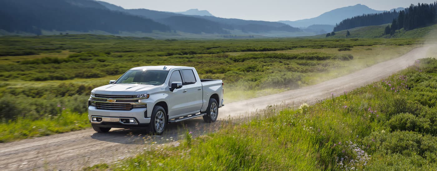 A white 2019 Chevy Silverado 1500 High Country is driving on a dirt trail after visiting an Oklahoma used Chevy truck dealer.