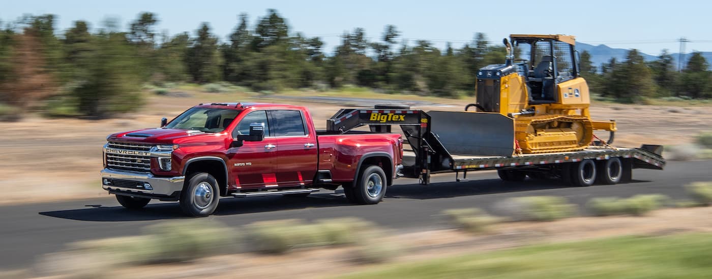 A red 2021 Chevy Silverado 3500 is shown towing heavy machinery. 