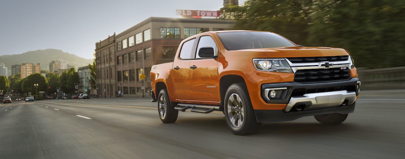 An orange 2021 Chevy Colorado Z71 is shown from the side driving through a city.