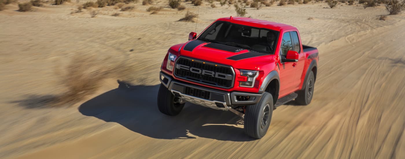 A red and black 2021 Ford F-150 Raptor is shown off-roading in a desert after looking for pre-owned luxury truck sales.