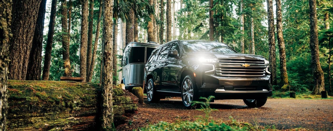 A black 2021 Chevy Tahoe High Country is shown towing an Airstream trailer on a path in the woods.