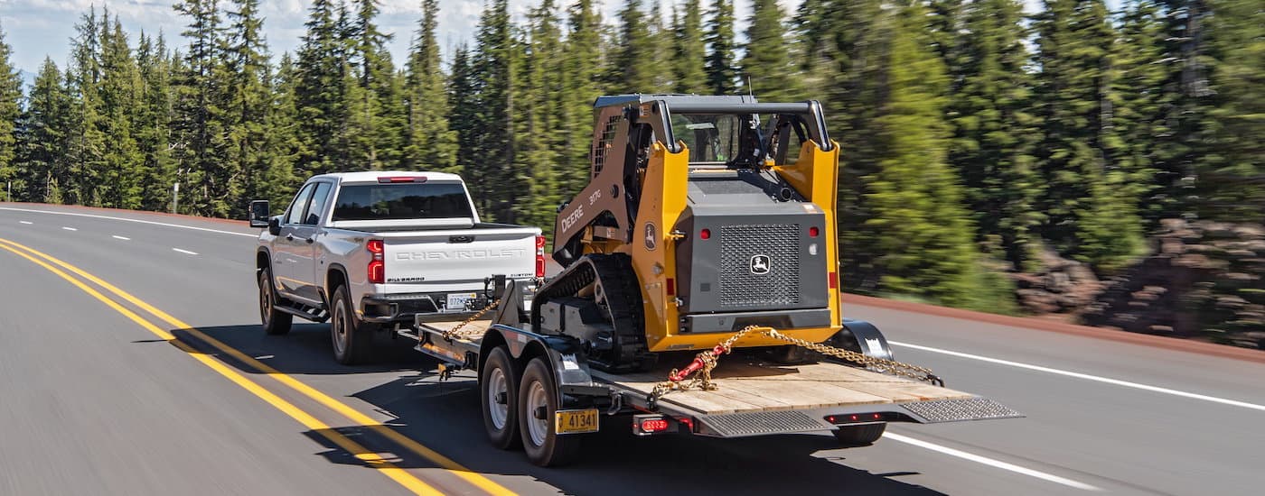 A white 2020 Chevy Silverado 2500HD is shown towing heavy machinery.