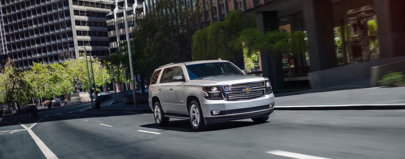 A silver 2020 Chevy Tahoe is shown driving on a city street by a used car dealer near you.