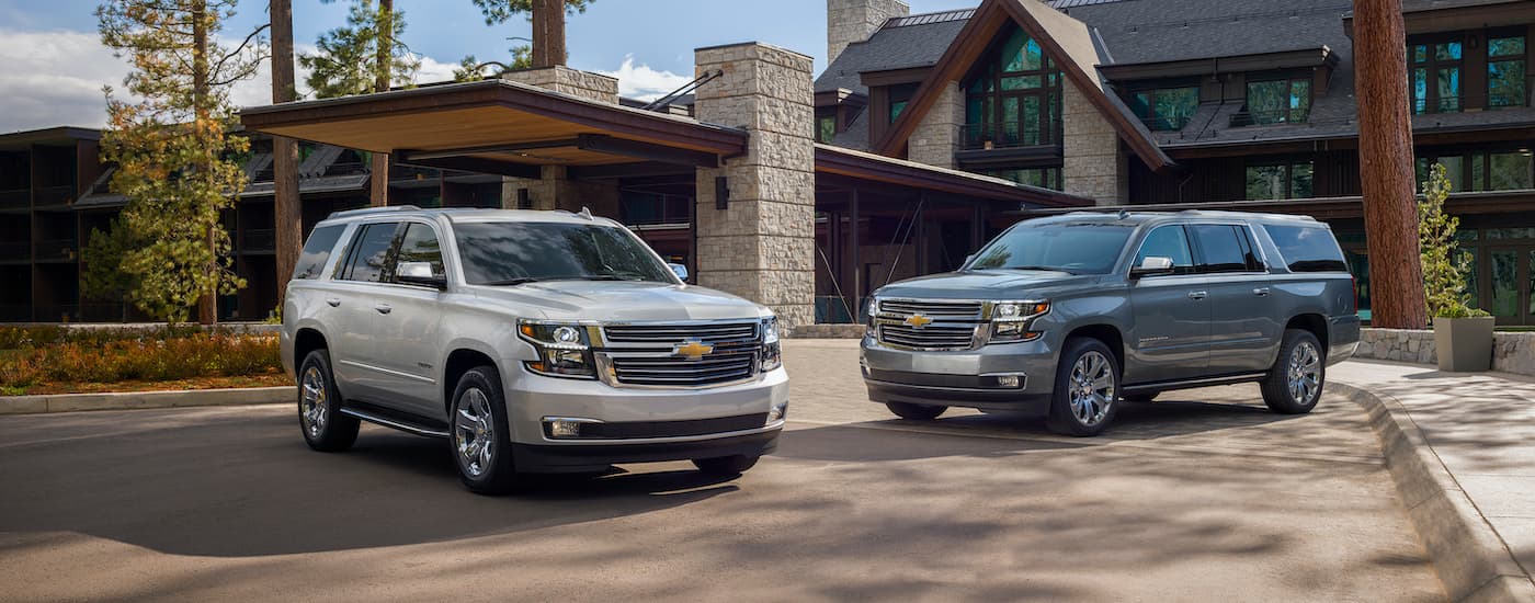 A silver 2020 Chevy Tahoe and a grey Suburban Premier Plus are shown in front of a cabin.