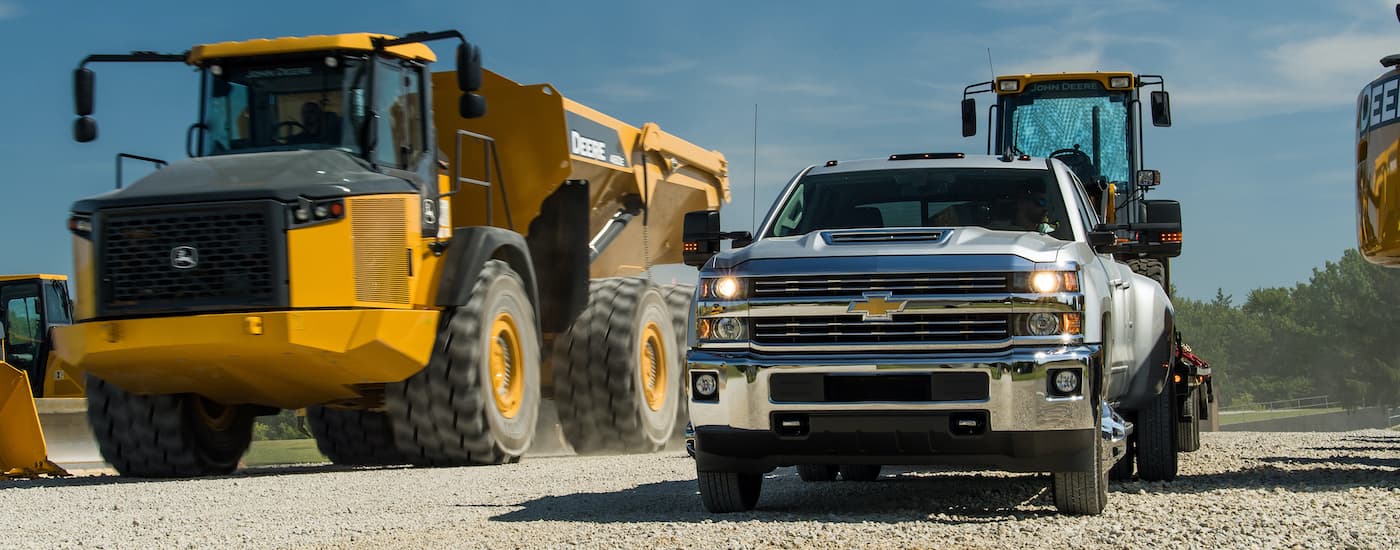 A silver 2018 Chevy Silverado 3500HD is shown towing heavy machinery after looking at used Chevrolet trucks.