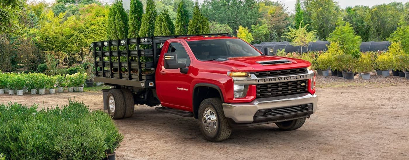 A red 2021 Chevy Silverado 3500 HD Chassis Cab is shown from the side parked at a plant nursery.
