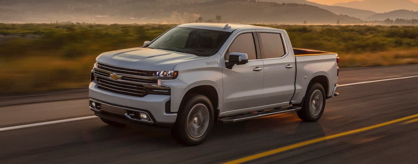A white 2019 Chevy Silverado 1500 is shown driving on a highway after visiting a used truck dealer.