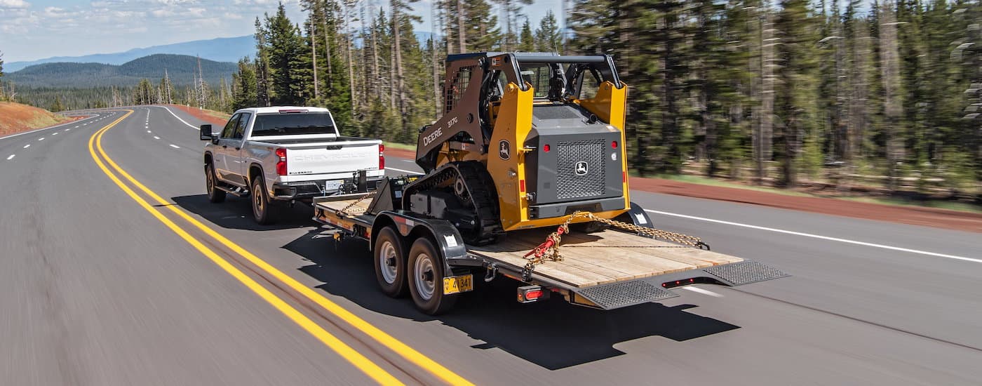 A white 2021 Chevy Silverado 2500HD is shown from the rear towing construction equipment.