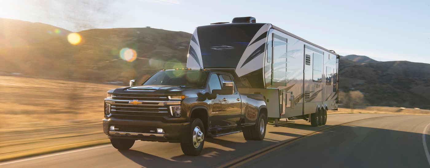 A black 2021 Chevy Silverado 3500HD is shown towing a trailer after leaving a used truck dealer near you.