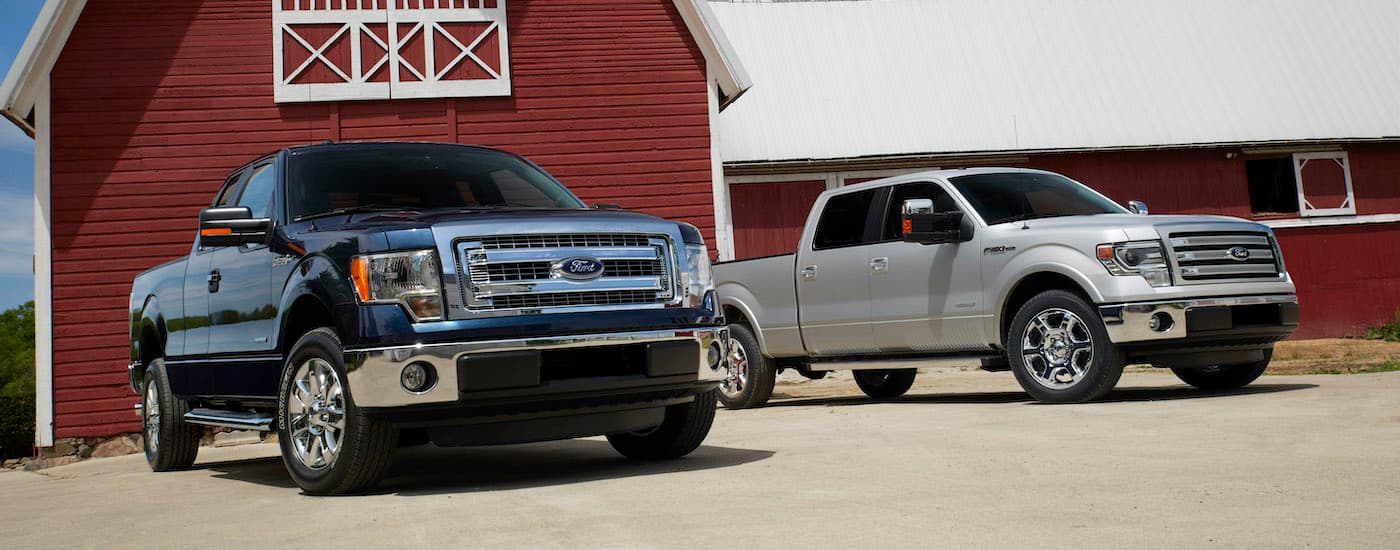 A black 2014 Ford F-150 XLT and a silver Lariat are shown parked in front of a barn.