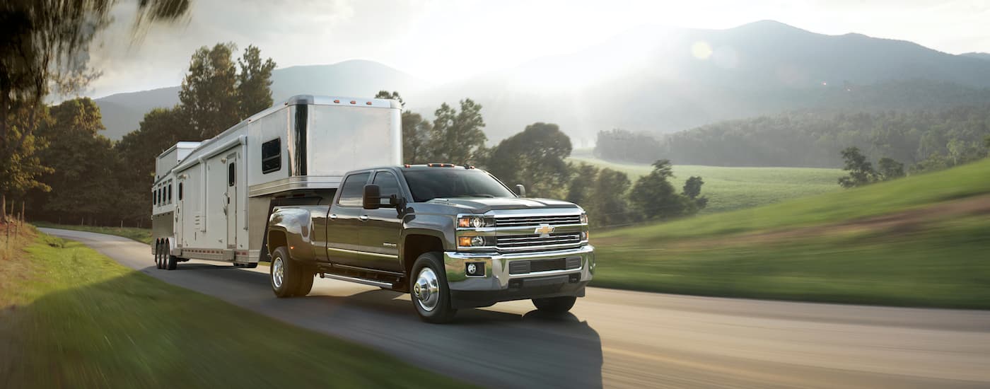 A popular used truck for sale, a grey 2016 Chevy Silverado 3500HD, is shown towing a trailer past a field.