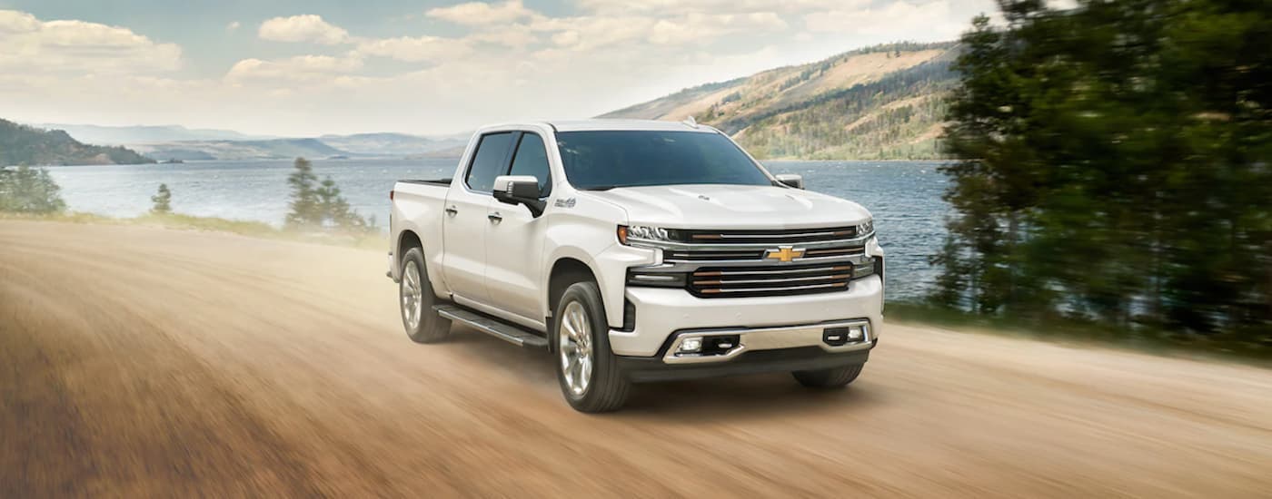 A white 2021 Chevy Silverado 1500 is shown from the front driving on a dirt road after searching for a used truck for sale.