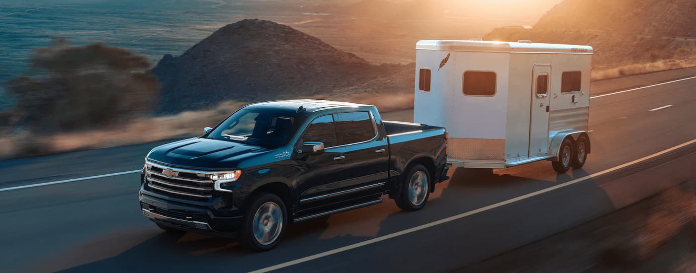 A black 2022 Chevy Silverado High Country is shown towing a trailer on an open road.