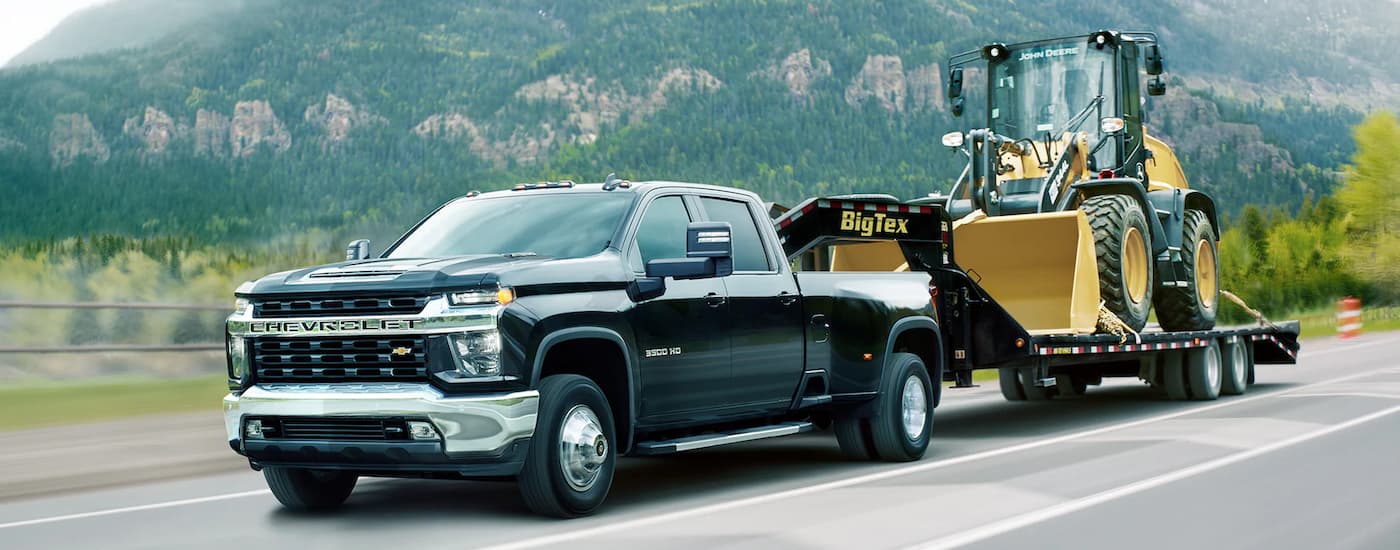 A black 2021 Chevy Silverado 3500HD WT is shown towing heavy machinery after leaving a diesel truck dealership.