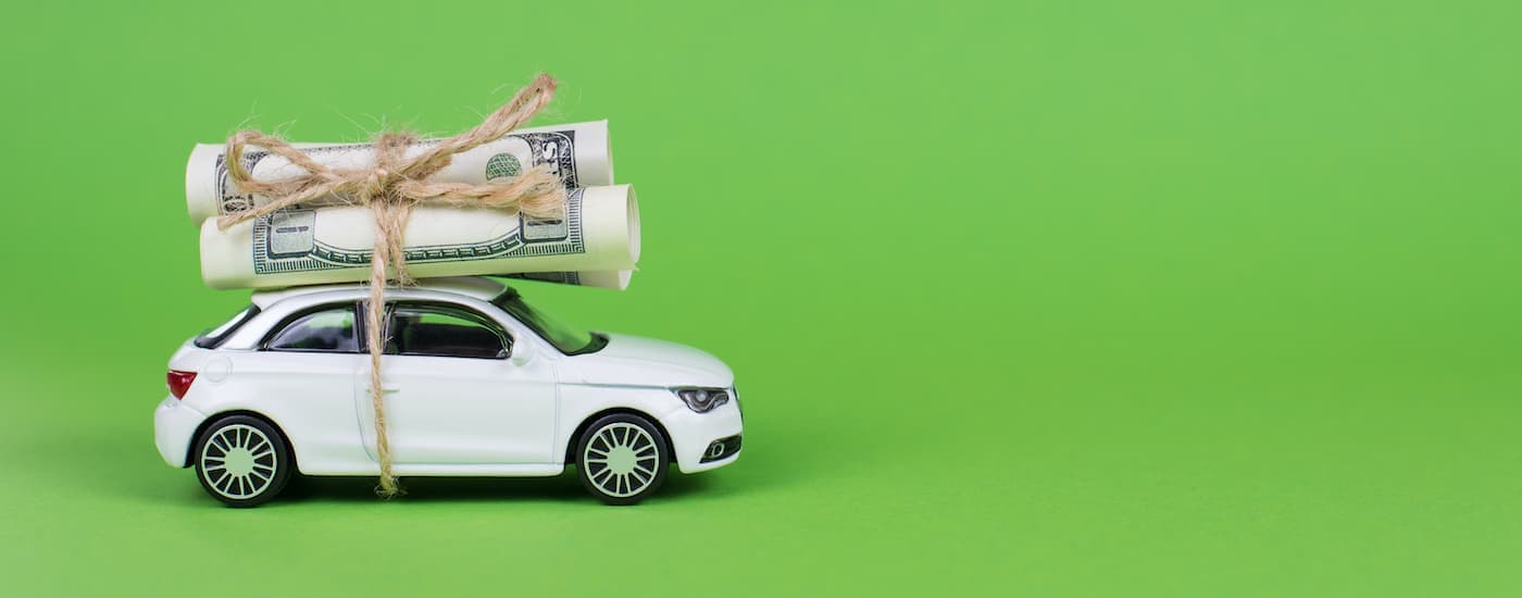 A white toy car is shown with cash tied to the roof.