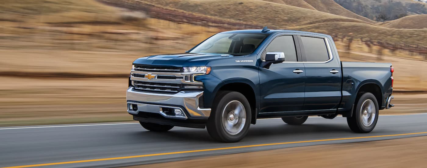 A blue 2021 Chevy Silverado 1500 is shown from the side driving on an open road.