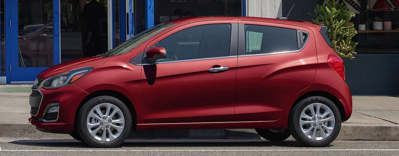A red 2022 Chevy Spark is shown from the side parked in front of a city building after leaving a Claremore Chevy dealer.