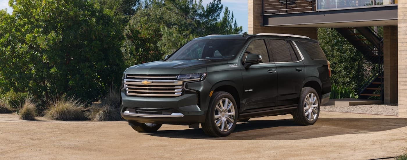 A green 2022 Chevy Tahoe is shown from the side parked in front of a house.