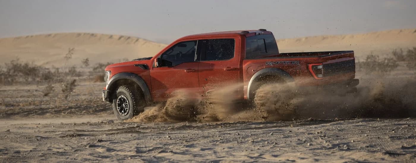 A red 2021 Ford F-150 Raptor is shown driving from the side after leaving a Oklahoma used Chevy truck dealer.