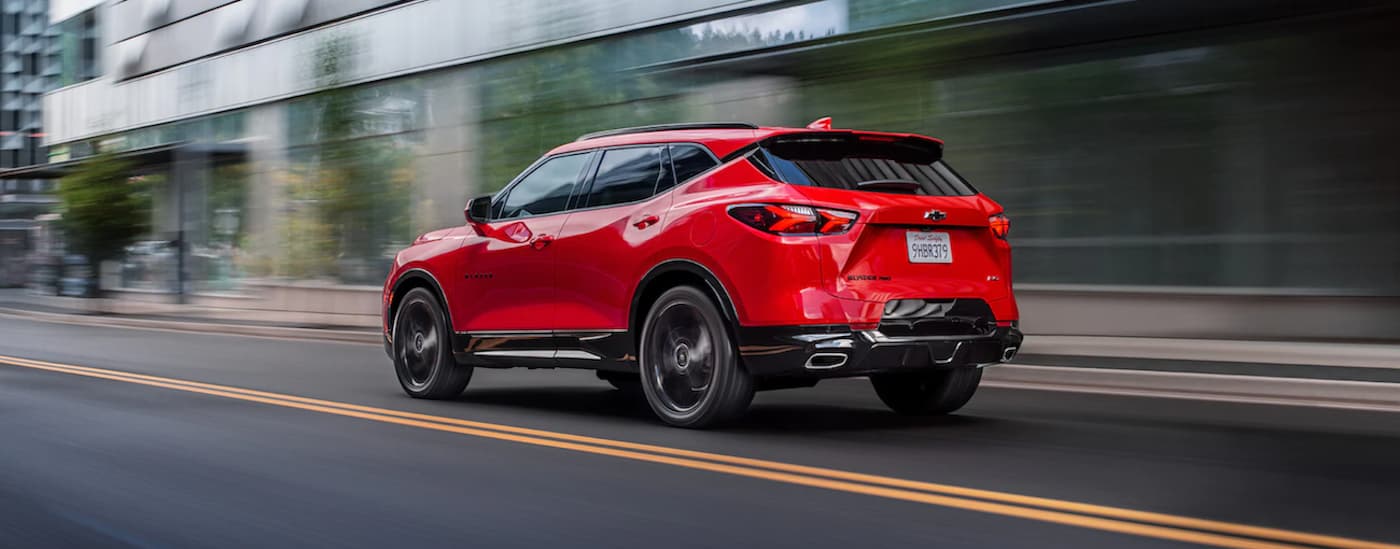A red 2021 Chevy Blazer is shown from the side driving through a city after leaving a used car lot.