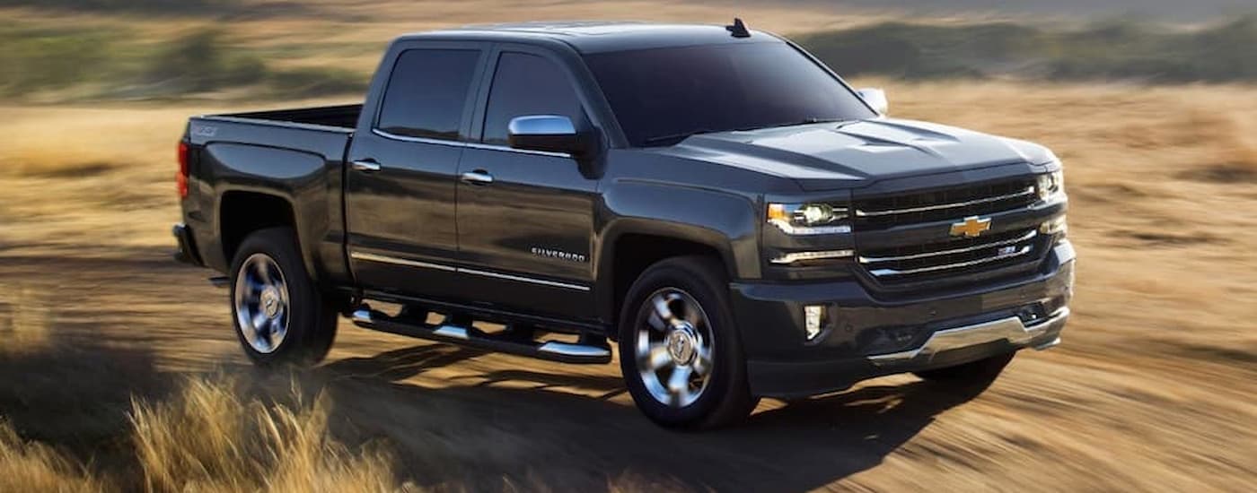 A black 2018 Chevy Silverado 1500 is shown driving on a dirt road.