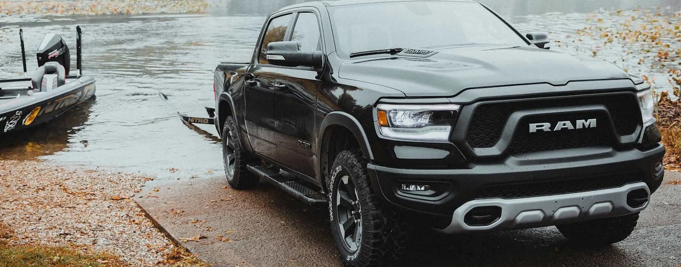 A black 2022 Ram 1500 is shown towing a boat trailer out of a lake.