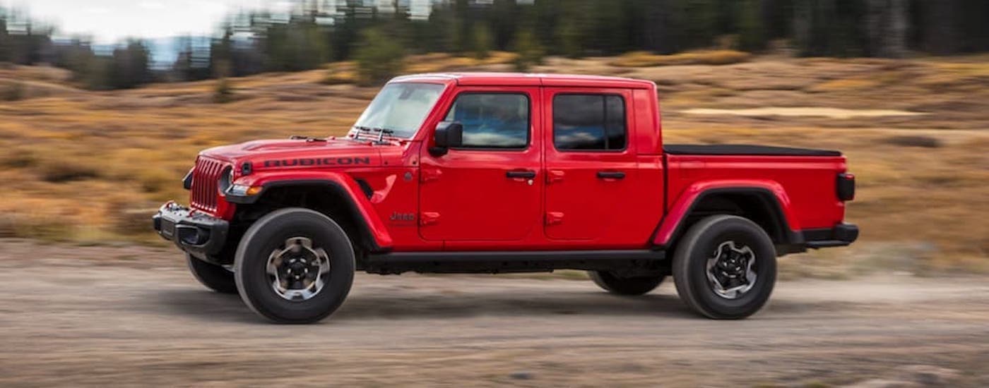 A red 2020 Jeep Gladiator is shown from the side driving on an open road after leaving a used truck dealer.